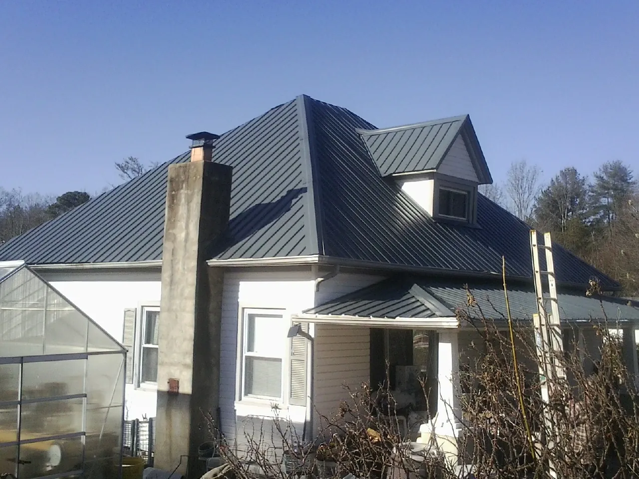 Dark blue standing seam metal roof on a white farmhouse with dormer — Slate & Tile Roof Repair by Roofing Brothers in Nordman