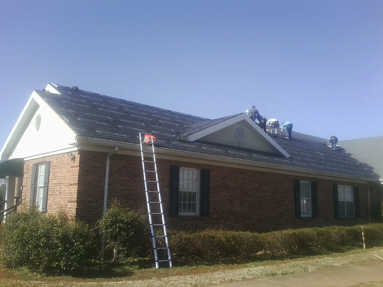 Crew tearing shingles off a brick ranch roof with a ladder set — Emergency Roof Repair work by our crew in Nordman