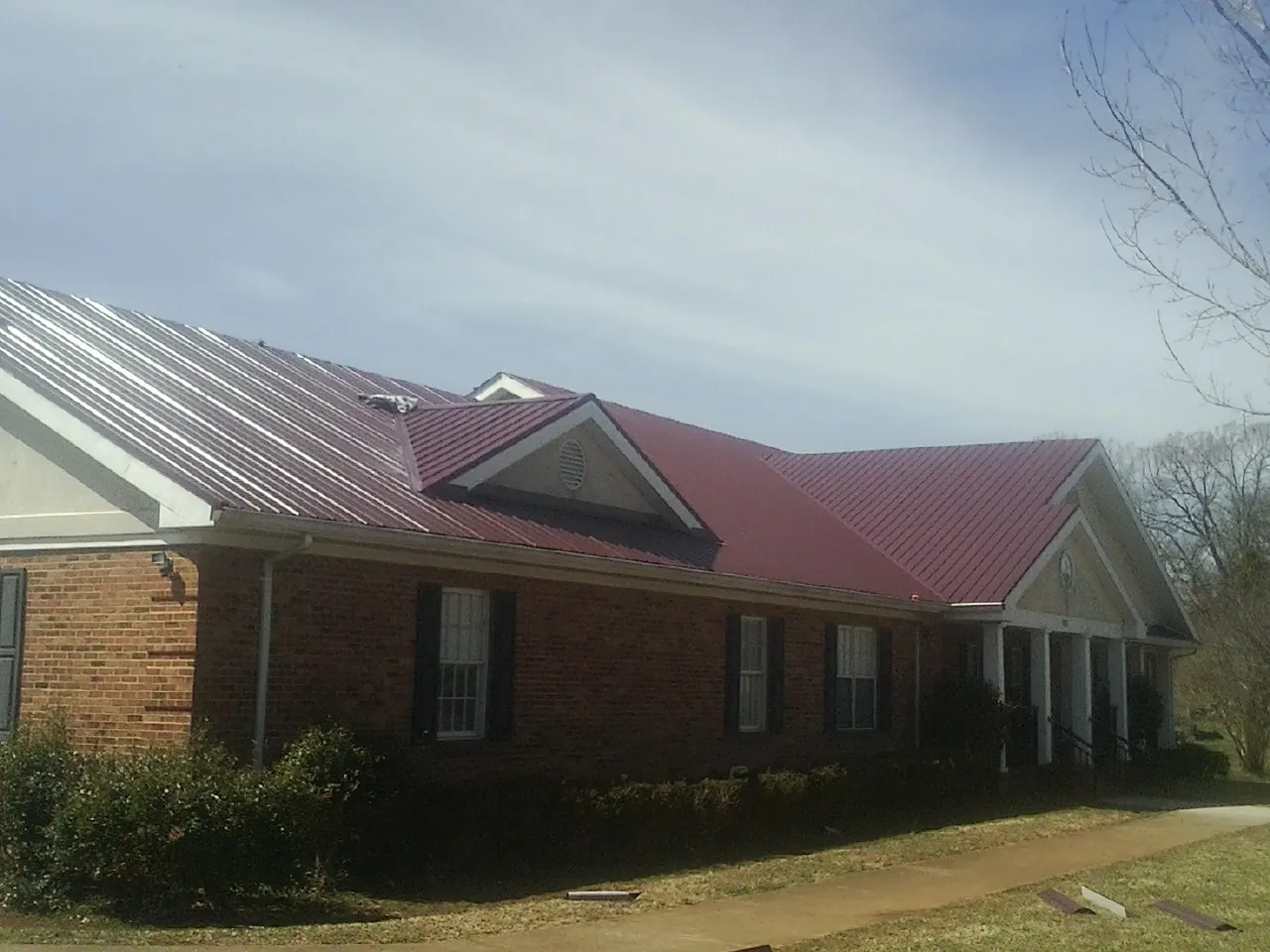 Red metal roof with gabled entries on a long brick building, from a Hail Damage Roof Repair job in Nordman