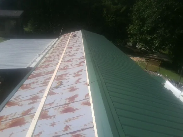 Old rusted panels beside newly installed green metal roofing — Wind Damage Roof Repair by Roofing Brothers in Nordman