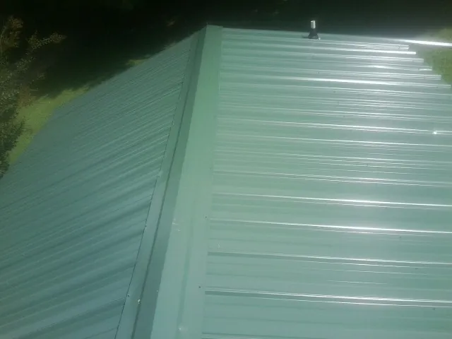 New green metal panels meeting at the ridge of a roof — Flat Roof Repair work by our crew in Nordman