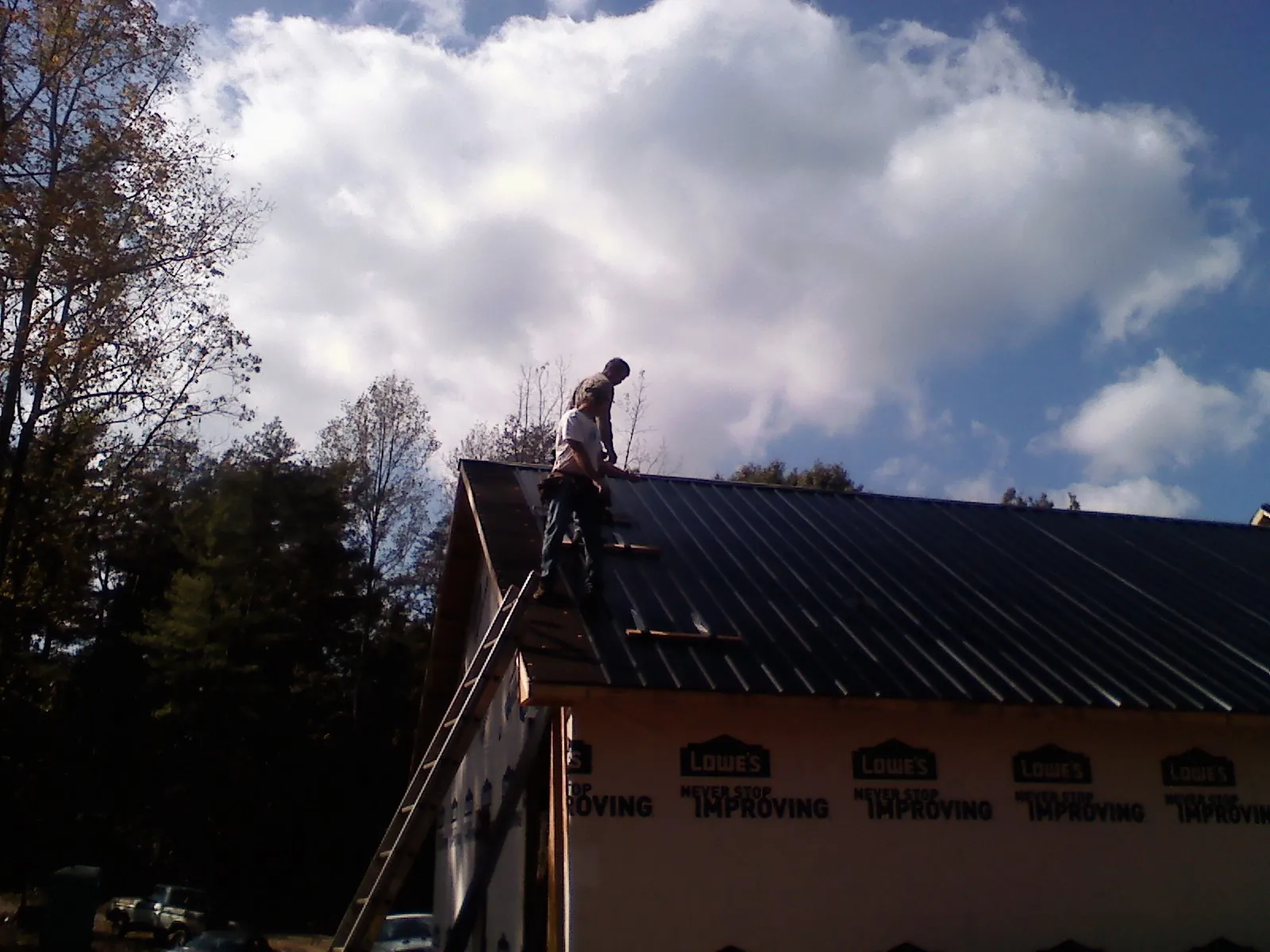 Roofer fastening dark metal panels high against a cloudy sky, from a Roof Inspection job in Nordman
