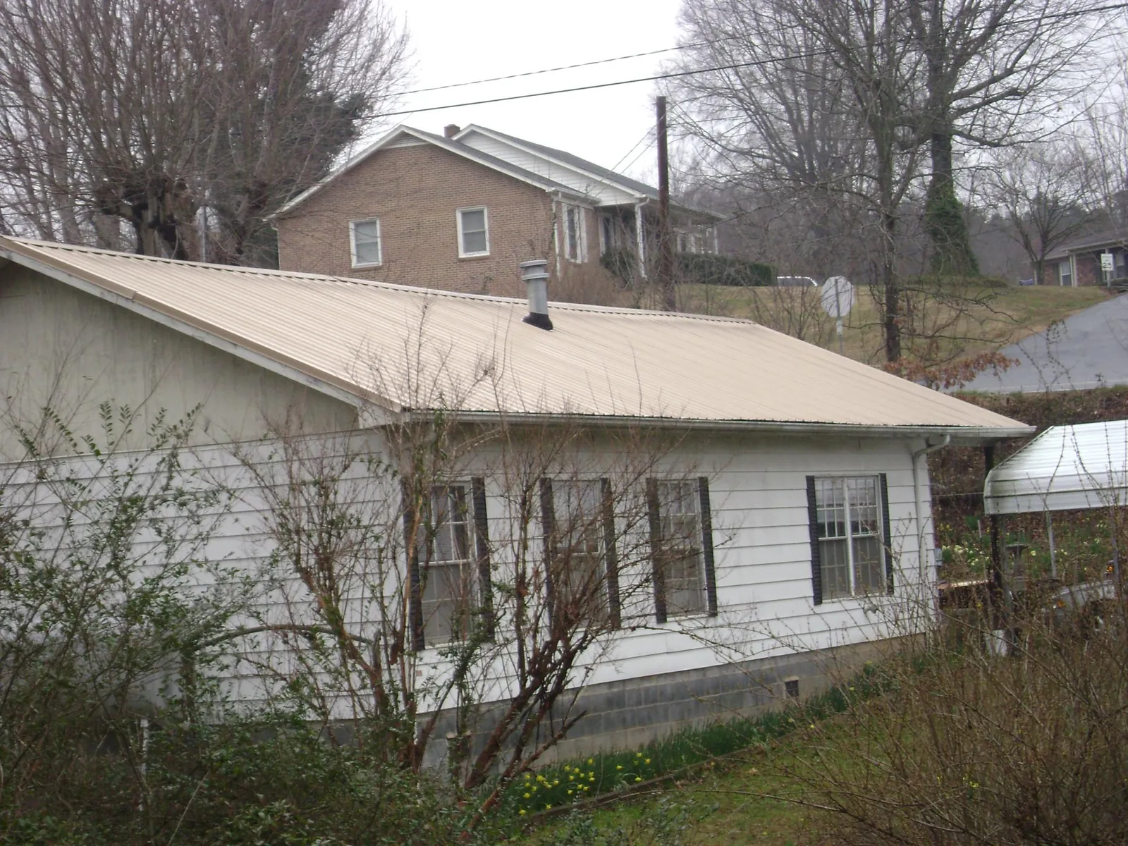 Tan metal roof on a white sided house set into a hillside — Commercial Roofing by Roofing Brothers in Nordman